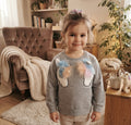 Sweat fille gris chiné avec deux têtes de licorne en relief et crinières pastel, porté